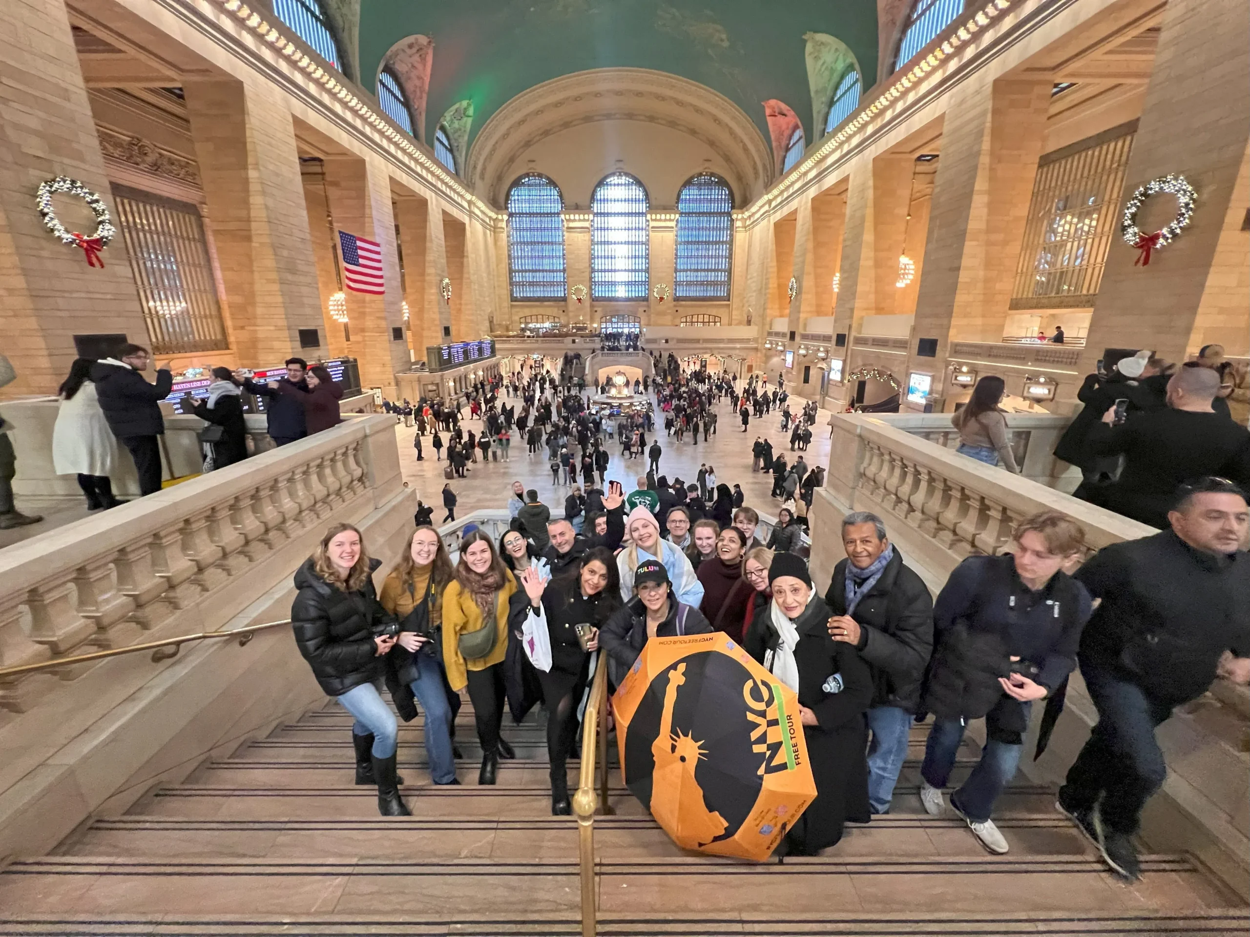 Group of people posing on stairs with an umbrella in Grand Central Terminal.