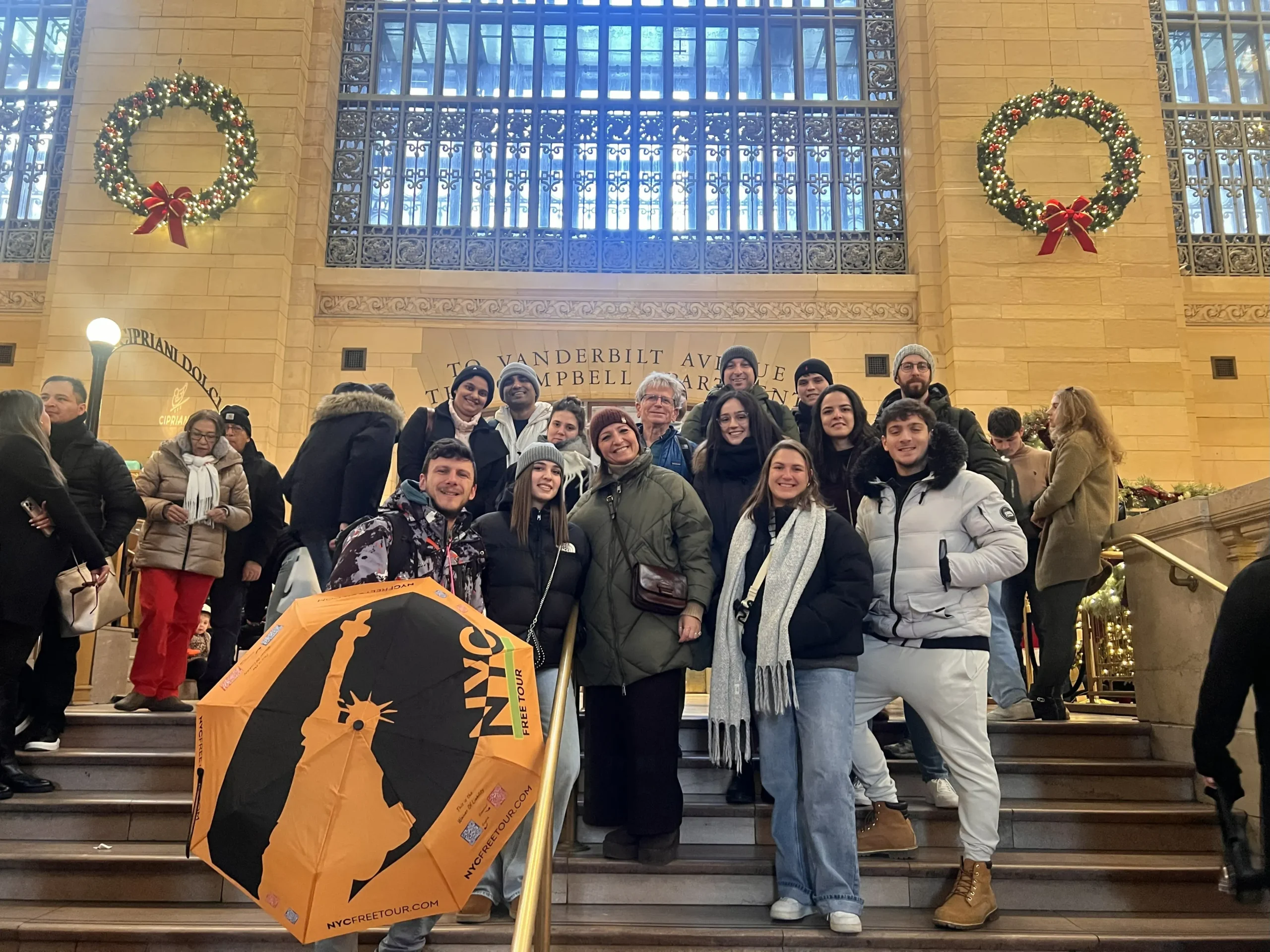 Group of people posing on stairs at Grand Central Terminal, decorated for the holidays.