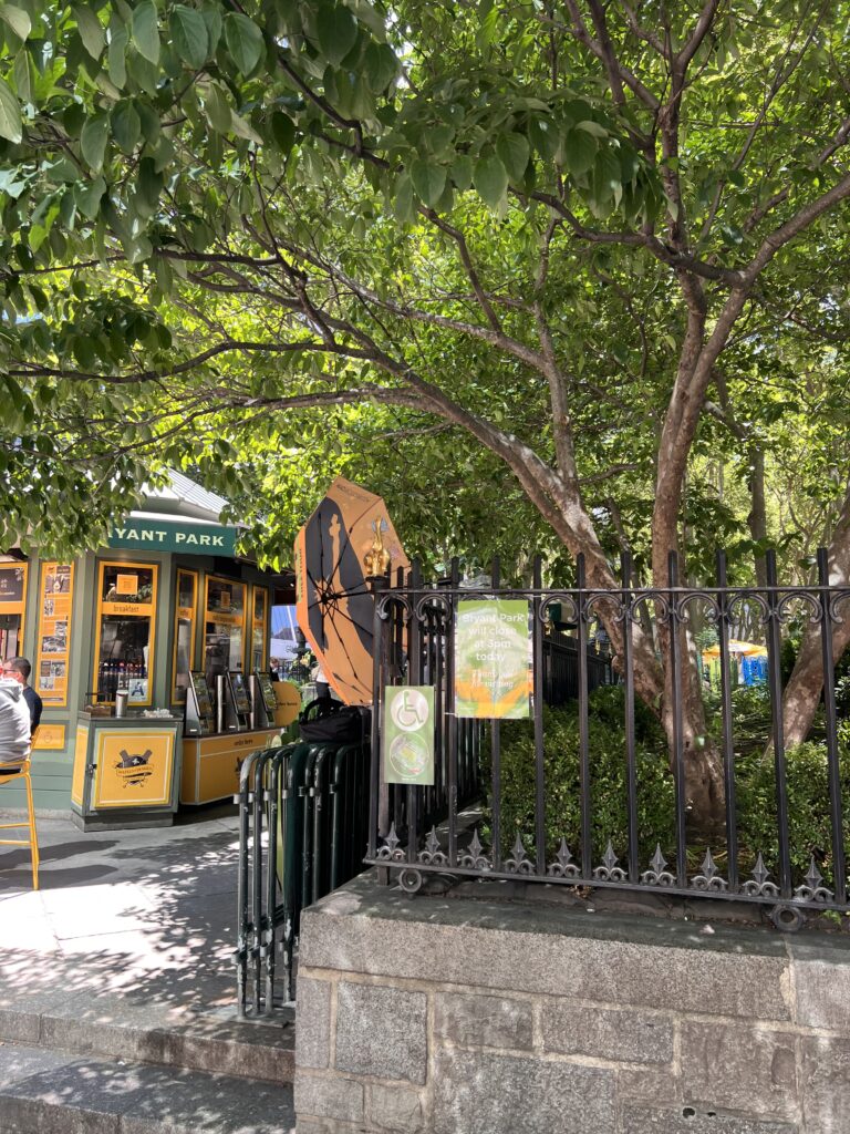 Orange-and-black Statue of Liberty umbrella hanging on the Bryant Park fence next to the Wafels & Dinges kiosk